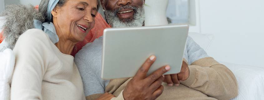 Front view of diverse senior couple using a digital tablet on sofa in beach house. Authentic Senior Retired Life Concept. online presence