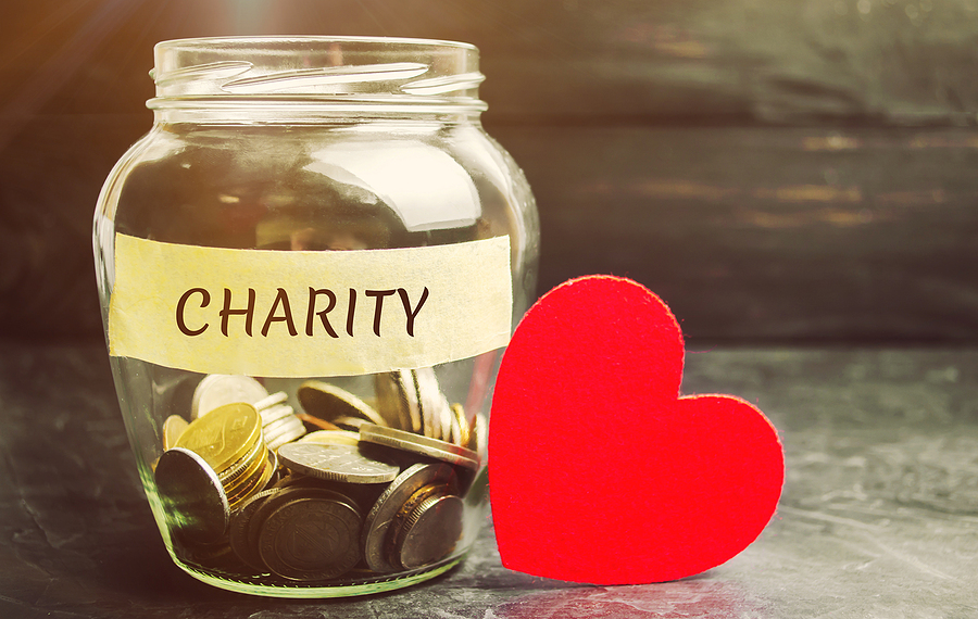 A jar labeled "charity" filled with coins next to a red heart, symbolizing charitable donations.